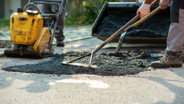 Construction workers apply a new layer of asphalt with rakes over a section of the road.