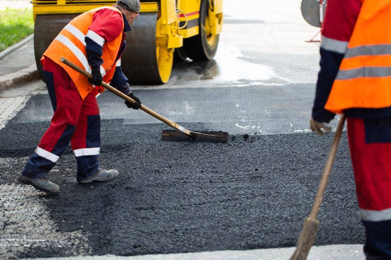 Construction workers applying a fresh coat of asphalt to the road.
